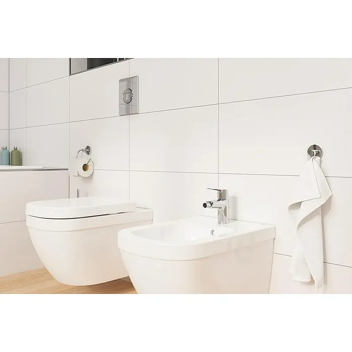 Grohe Start Bidetarmatur S-Size - Chrom, Glänzend - Elegantes Badezimmer mit einer modernen Toilette und Bidet, ergänzt durch Armaturen und einem Handtuch, die den Fokus auf hochwertige Sanitärkeramik legen.