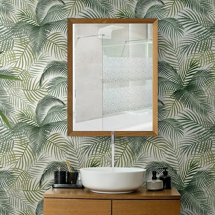 Papel pintado de vinilo autoadhesivo Tropical - Verde, L x An: 280 x 65 cm - El baño cuenta con un lavabo sobre un mueble de madera, un espejo y una pared con un estampado de hojas tropicales.