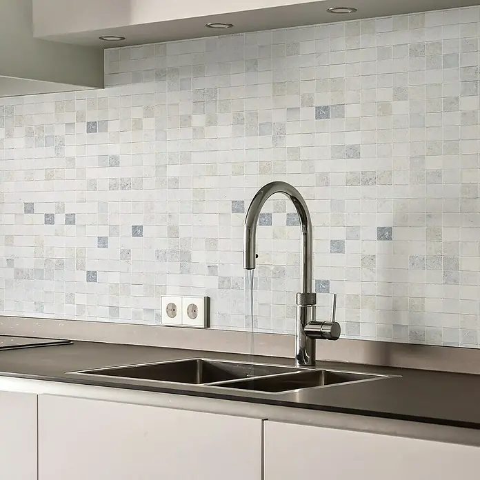 Papel pintado de vinilo autoadhesivo Mármol - Blanco, L x An: 280 x 65 cm - Primer plano de un fregadero de cocina con un protector contra salpicaduras de azulejos de mosaico. El grifo está abierto y el diseño de los azulejos añade un toque de textura a la cocina.