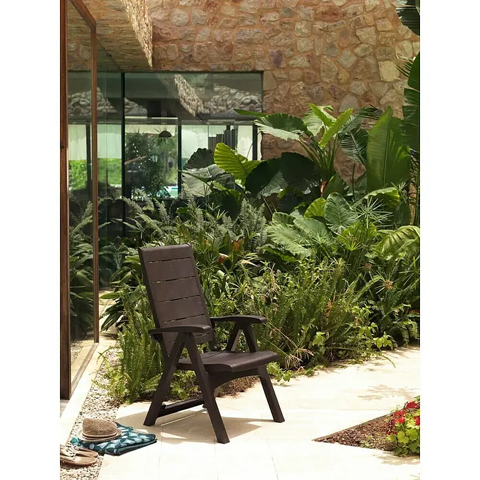 Sillón de posiciones Legno - 65 x 63 x 108 cm, Marrón, Polipropileno, Respaldo regulable - Silla de jardín marrón de plástico en un patio con vegetación exuberante. Perfecto para relajarse al aire libre.