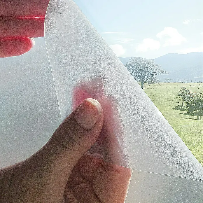 Lámina para ventana de vinilo Cosmos - 67,5 cm x 2 m, Transparente - Primer plano de una persona que sostiene una lámina de vidrio esmerilado que proporciona privacidad y permite el paso de la luz.