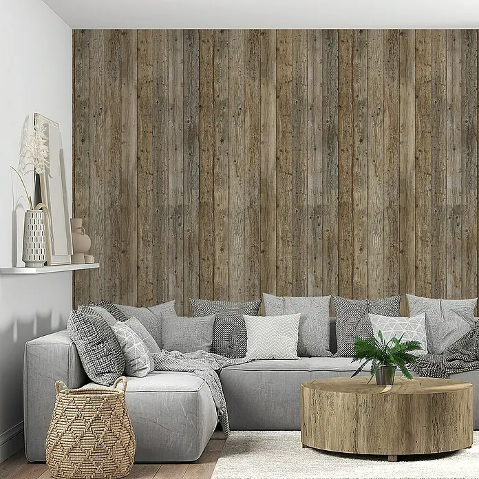 Lámina decorativa autoadhesiva vinílico Premium - 90 x 280 cm, Tablón viejo, Marrón - Interior con una pared de madera al fondo, con un sofá gris con cojines y una mesa de centro redonda delante.