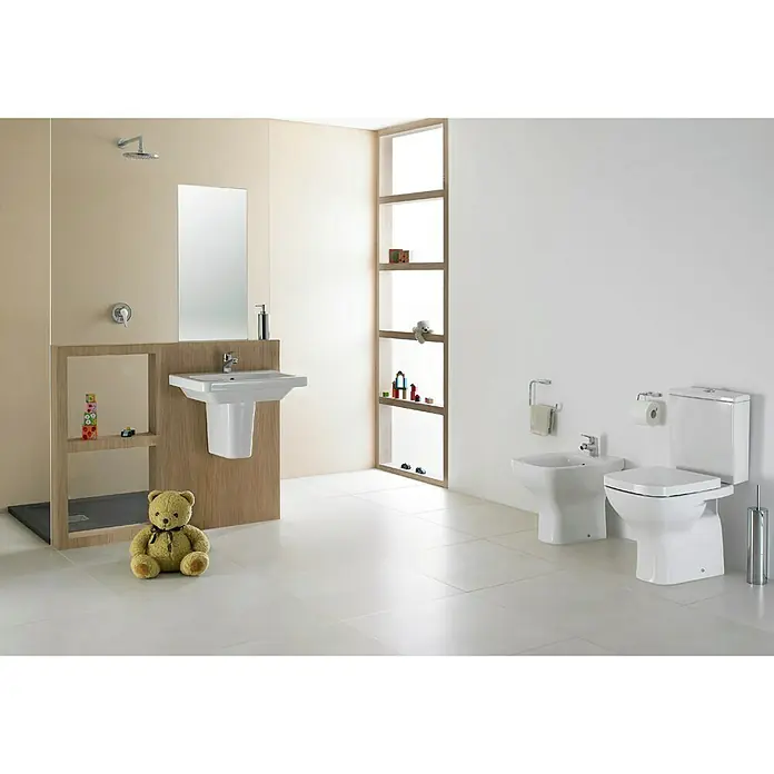 Gala Street Square Tapa de WC - Blanco, Con caída amortiguada - Un baño luminoso con un inodoro de cerámica blanca, un bidé y un lavabo. Un osito de peluche está sentado en el espacio, añadiendo un toque infantil.