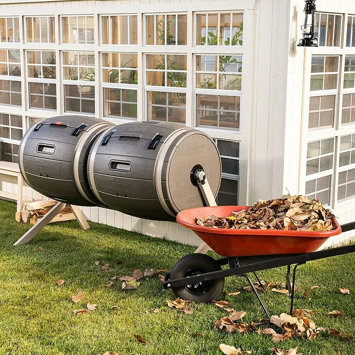 Lifetime Komposter Doppelfass - 380 l, 79 x 160 x 110 cm - Zwei rotierende Kompostbehälter aus Kunststoff im Garten mit einer Schubkarre voller Blätter.