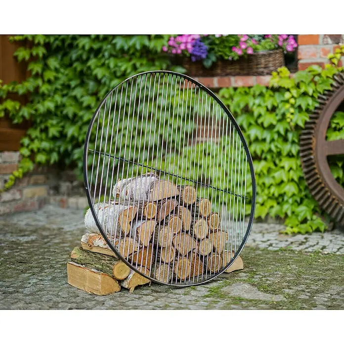 CookKing Grillrost - Durchmesser: 70 cm, Stahl - Rundes Metall-Grillrost, silber mit schwarzem Rand, an einem Holzstapel gelehnt.