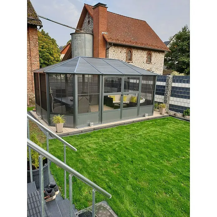 Sojag Standard-Pavillon Charleston 1212 - B x T: 383,6 mm x 383,6 cm, Anthrazit, Aluminium - Ein grauer Gartenpavillon mit Wellblechdach und teils transparenten Wänden, mit Gartenmöbeln innen, auf einer Terrasse im Garten.