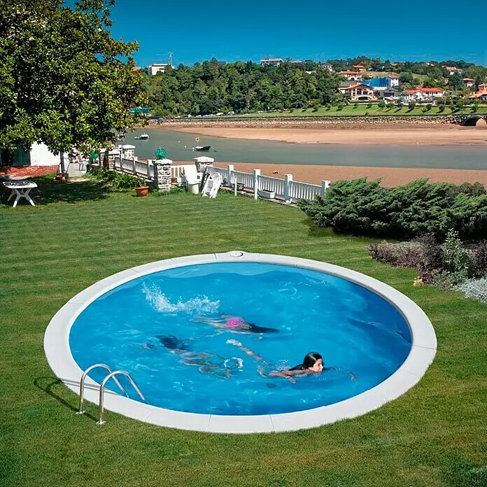 Gre Kit de piscina enterrada Madagascar - L x An x Al: 420 x 420 x 150 cm, 18.840 l - Piscina circular enterrada con agua azul y borde blanco, instalada en un exuberante jardín verde con gente nadando.