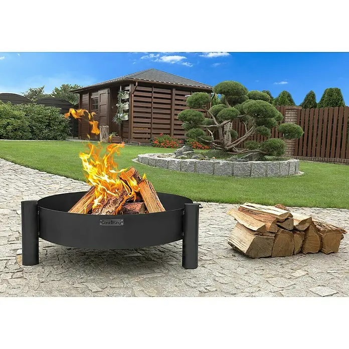 CookKing Feuerschale Haiti - Durchmesser: 80 cm, Stahl - Schwarze Metall-Feuerschale mit brennendem Holz und Holzstapel auf Steinterrasse im Garten.