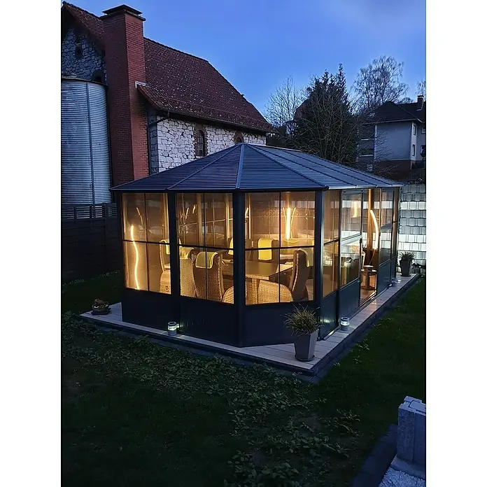 Sojag Standard-Pavillon Charleston 1212 - B x T: 383,6 mm x 383,6 cm, Anthrazit, Aluminium - Beleuchteter dunkelgrauer Gartenpavillon mit Glaswänden und dunkelgrauem Dach, zeigt einladende Innenmöbel bei Dämmerung.
