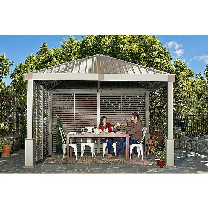 Sojag Standard-Pavillon Nanda 1212 - B x T: 363 x 363 cm, Champagner, Aluminium - Ein Metall-Hardtop-Pavillon mit Lamellenwänden bietet einem Paar einen schattigen Essbereich im Freien.