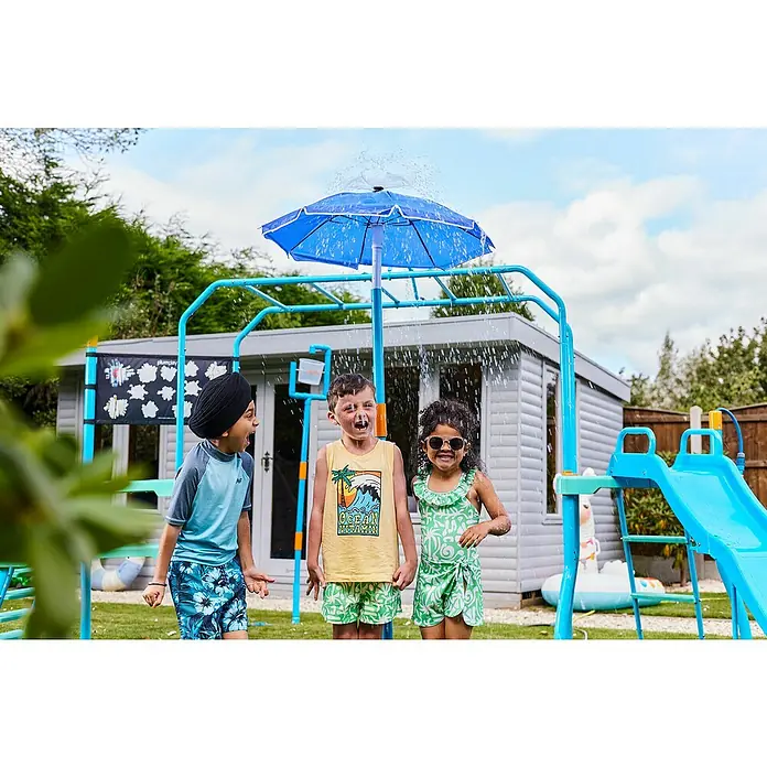 Plum Wasserspiel Water Park Wasserschirm-Fontäne - Blau - Blaues Wasser-Spielgerüst mit Sprinkler und Rutsche, von drei Kindern im Garten genutzt.