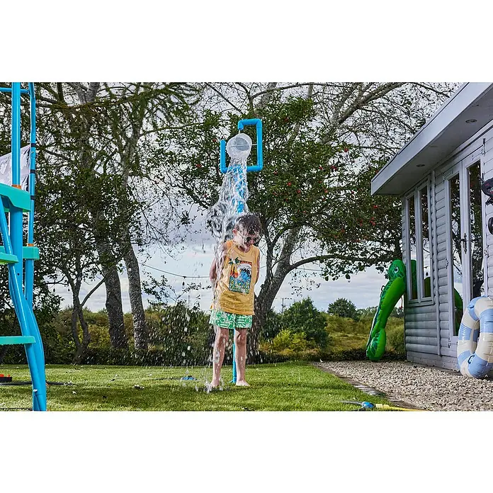 Plum Kinderspielturm Water Park Eimer Dusche - Blau - Ein Kind steht unter einem blauen und transparenten Wasserspielbogen aus Kunststoff, der Wasser sprüht.