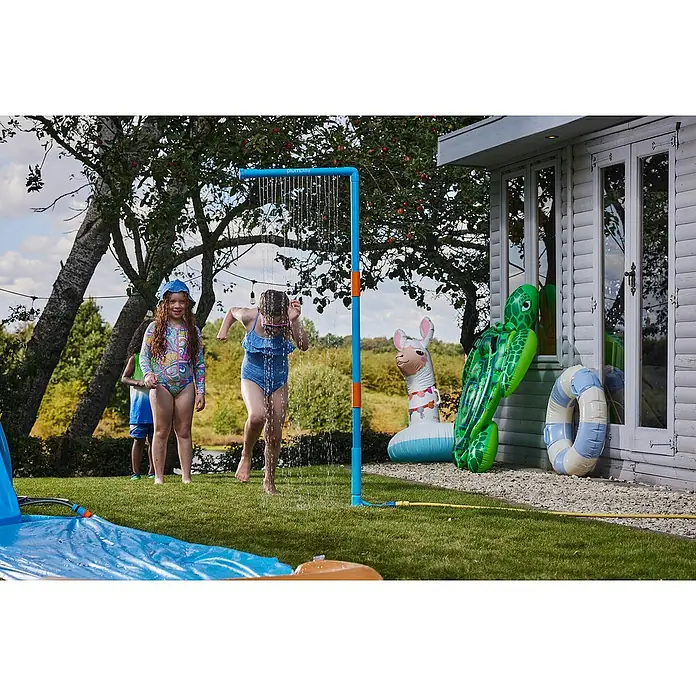 Plum Kinderspielturm Water Park Wasservorhang - Blau - Ein Kind spielt unter einer blau-orangen Gartendusche, die in einem sonnigen Garten aufgestellt ist.