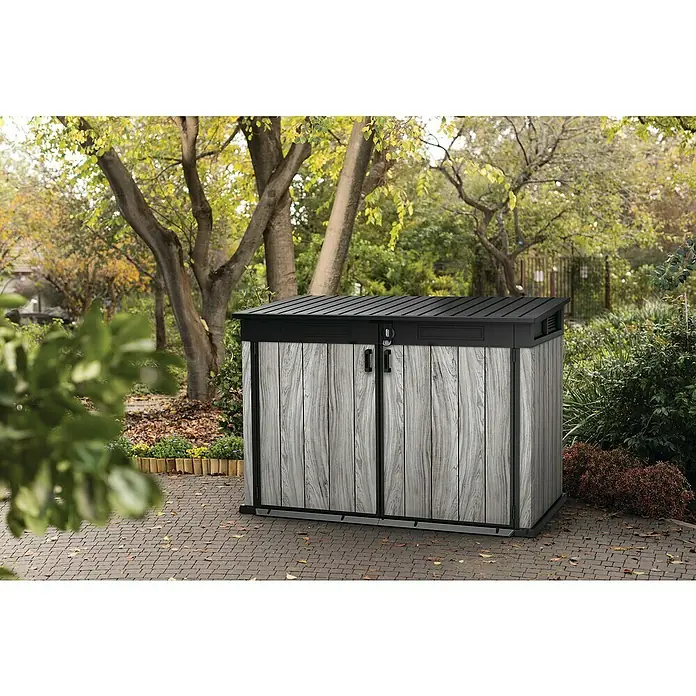 Keter Garten-Aufbewahrungsbox Signature Storm Grey Grande-Store - Außenmaß inkl. Dachüberstand (B x T): 190 x 109 cm, Kunststoff, Stormgrey - Graues Gartenhaus in Holzoptik mit schwarzem Dach und Zierleisten auf gepflasterter Terrasse im Garten.
