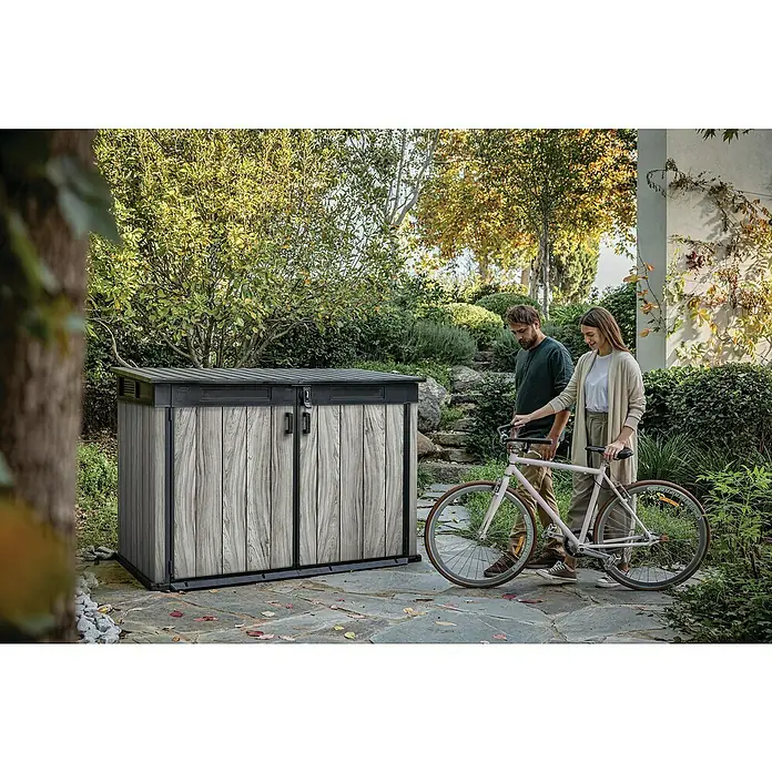 Keter Garten-Aufbewahrungsbox Signature Storm Grey Grande-Store - Außenmaß inkl. Dachüberstand (B x T): 190 x 109 cm, Kunststoff, Stormgrey - Großer Outdoor-Lagerschuppen mit dunkelgrauen und Holzmaserungsplatten, im Garten mit Personen und Fahrrad.