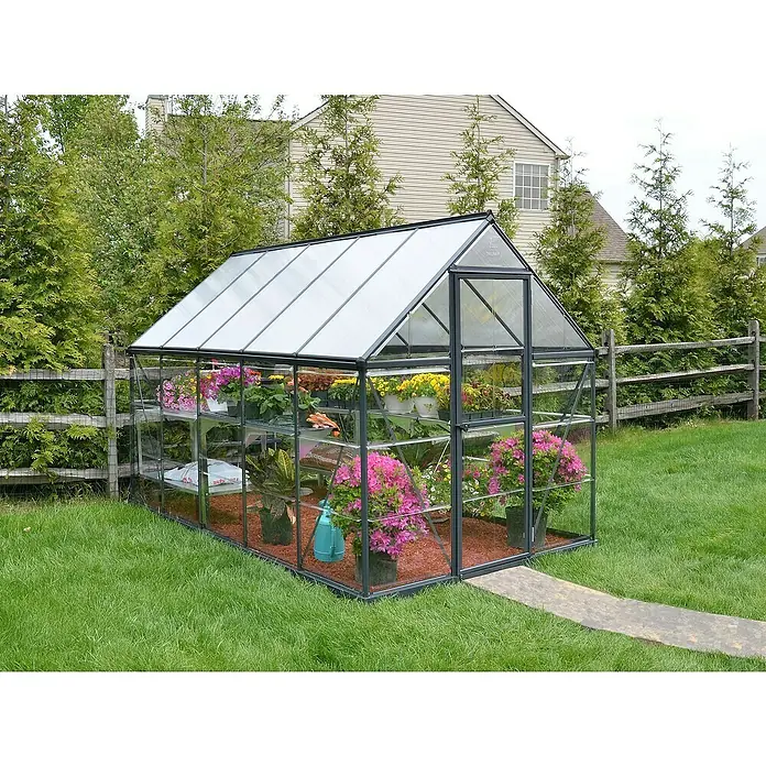 Palram – Canopia Gewächshaus Hybrid - Außenmaß inkl. Dachüberstand (B x T): 185 x 306 cm, 0,7 mm, Anthrazit - Ein Gewächshaus mit Pflanzen und Blumen, umgeben von Rasen und Bäumen im Garten. Das Gewächshaus bietet optimalen Schutz für Pflanzen.