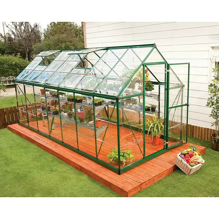 Palram – Canopia Gewächshaus Harmony - Außenmaß inkl. Dachüberstand (B x T): 185 x 426 cm, Grün, Grundfläche: 7,9 m² - Ein geräumiges Gewächshaus mit Glaswänden, gefüllt mit Pflanzen, steht auf einem Holzdeck in einem gepflegten Garten.