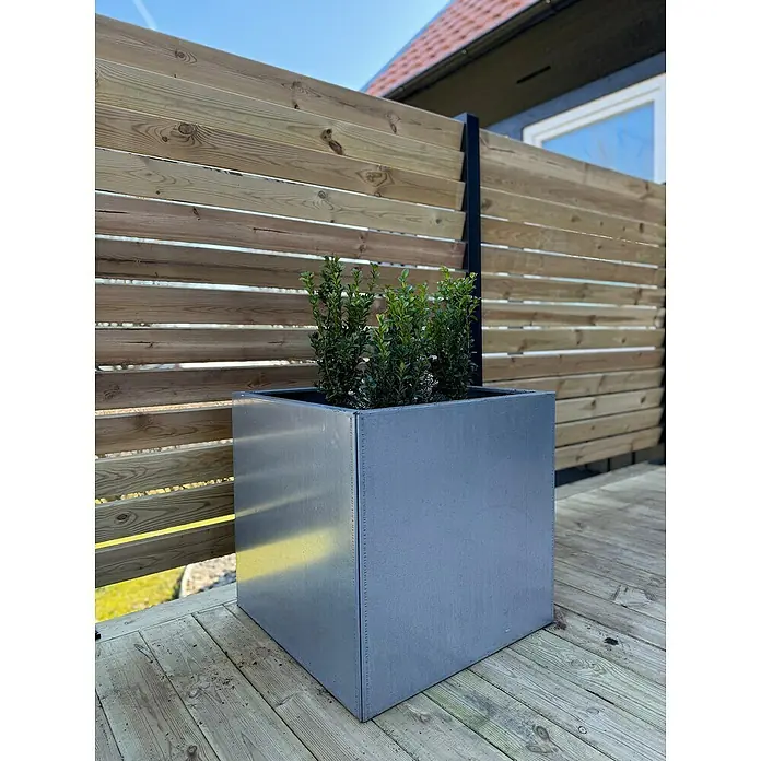 Recal Pflanzkübel eckig - Außenmaß (L x B x H): 55 x 55 x 55 cm, Stahl, Magnelis - Ein quadratischer, silbergrauer Pflanzkübel aus Metall mit grünen Pflanzen, der auf einer Holzterrasse vor einem Holzzaun steht.