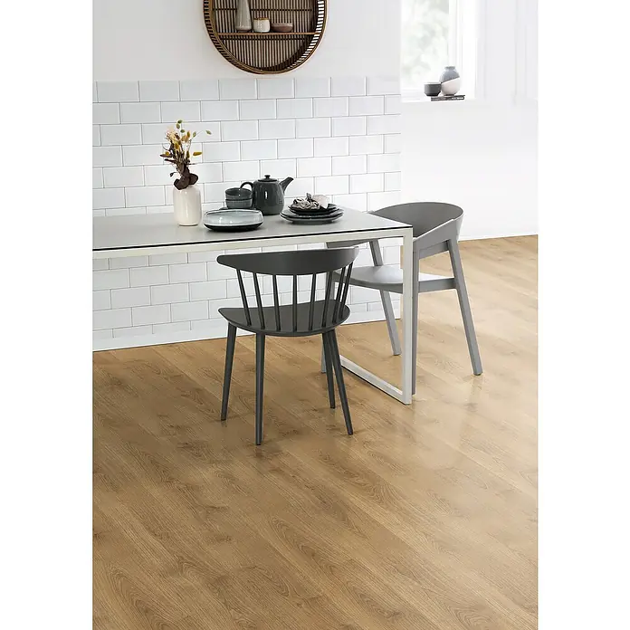 Egger Laminat NatureSense - Nord Eiche natur, Landhausdiele, 1.292 x 193 x 8 mm - Einrichtung mit einem Esstisch, Geschirr, zwei Stühlen und einem runden Regal an der Wand vor einer weißen, gefliesten Wand und einem Holzfußboden.