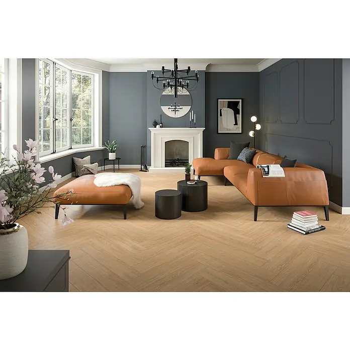 Egger Laminat NatureSense Herringbone - Casella Eiche natur, Fischgrät, 840 x 168 x 8 mm - Elegantes Wohnzimmer mit modernem Ledersofa, stilvollen Couchtischen und einem hellen, attraktiven Fischgrätparkettboden.