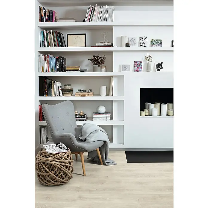 Egger Laminat NatureSense - Brook Eiche weiss, Landhausdiele, 1.292 x 193 x 7 mm - Ein gemütlicher Lesesessel mit Decke vor einem Bücherregal, perfekt für entspannte Stunden mit einem Buch.