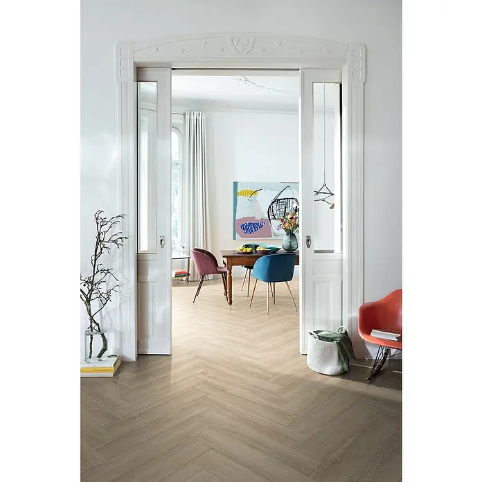 Egger Laminat NatureSense Herringbone - Newport Eiche creme, Fischgrät, 840 x 168 x 8 mm - Helle, moderne Diele mit Parkettboden in Fischgrätmuster, gesehen durch einen offenen Durchgang mit weißen Zargen. Elegantes, einladendes Ambiente.