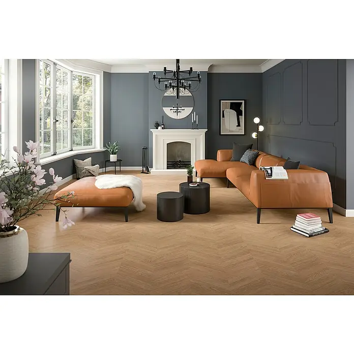 Egger Laminat NatureSense Skanderborg - Skanderborg Eiche braun, Sonstige, 1.292 x 327 x 8 mm - Ein Wohnzimmer mit einem braunen Ledersofa und passendem Ottomane auf einem hellen Holzboden. Über dem Sofa hängt eine moderne Lampe.