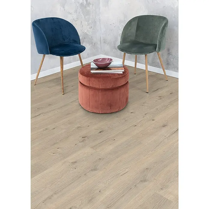Egger Laminat NatureSense - Murom Eiche, Landhausdiele, 1.292 x 193 x 8 mm - Zwei elegante Samtstühle in Blau und Grün stehen neben einem runden, rosafarbenen Ottoman mit Büchern und einer Schale darauf.