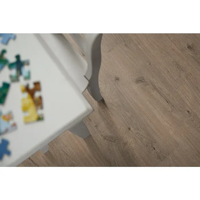 Egger Laminat NatureSense - Murom Eiche natur, Landhausdiele, 1.292 x 193 x 8 mm - Nahaufnahme von einem Kindertisch mit einem unvollständigen Puzzle auf einem hellbraunen Holzlaminatboden. Der Tisch hat geschwungene Beine.