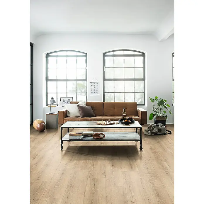 Egger Laminat NatureSense - Carlin Eiche sand, Landhausdiele, 1.292 x 246 x 8 mm - Wohnzimmer mit hellbraunem Laminatboden, braunem Sofa, Couchtisch und großen Fenstern.