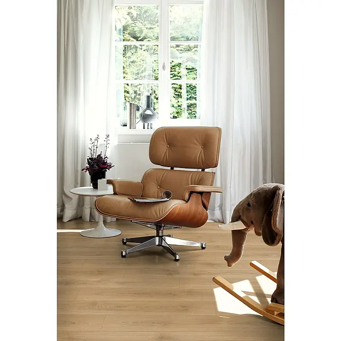 Egger Laminat NatureSense - Nord Eiche hellbraun, Landhausdiele, 1.292 x 193 x 8 mm - Ein stilvolles Interieur mit einem braunen Ledersessel, einem Beistelltisch und einem Schaukelelefanten vor einem hellen Fenster.