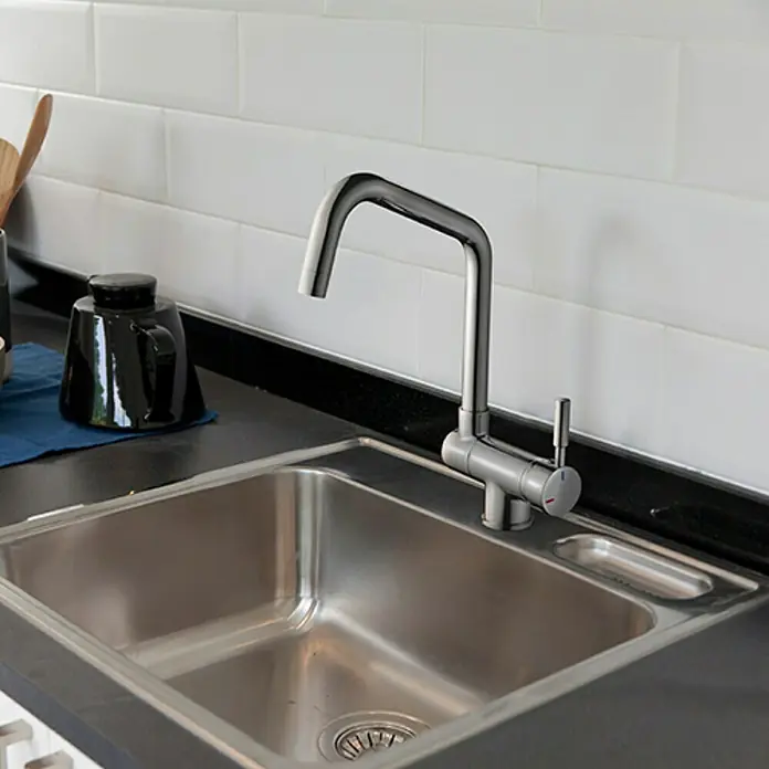 Rousseau Grifo de cocina Mica - Cromo - Primer plano de un fregadero de acero inoxidable con un moderno grifo cromado, sobre un fondo de pared de azulejos blancos. Un diseño de cocina elegante y funcional.
