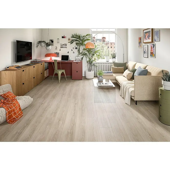 Egger Laminat NatureSense - Newport Eiche hellgrau, Landhausdiele, 1.292 x 193 x 7 mm - Ein helles Wohnzimmer mit Holzboden, beiger Couch und einem Schreibtisch mit orangener Lampe. Pflanzen und moderne Kunstwerke ergänzen das Interieur.
