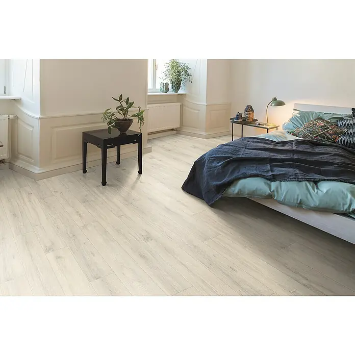 Egger Laminat NatureSense - Kreideeiche, Landhausdiele, 1.292 x 193 x 7 mm - Helles Schlafzimmer mit Laminatboden in Holzoptik, einem Bett mit blaugrüner Bettwäsche und einem schwarzen Beistelltisch mit Pflanze.