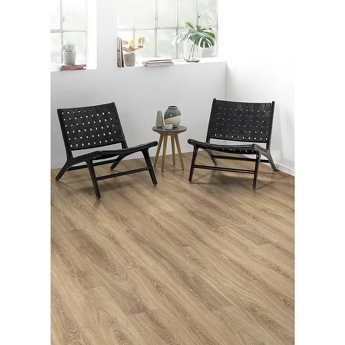 Egger Laminat NatureSense - Bardolino Eiche, Landhausdiele, 1.292 x 193 x 8 mm - Elegantes Interieur mit zwei schwarzen Rattansesseln und Holzboden, beleuchtet durch Fenster mit Topfpflanzen.