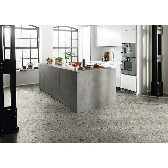 Egger Laminat NatureSense Aqua - Triestino Terrazzo grau, 1.292 x 327 x 8 mm - Moderne Küche mit einer Kücheninsel aus Beton und weißen Schränken. Der Boden ist mit grauem Terrazzo belegt und große Fenster sorgen für Helligkeit.