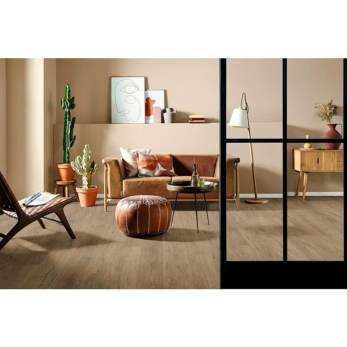 Egger Laminat NatureSense Aqua - Melba Eiche braun, Landhausdiele, 1.292 x 193 x 8 mm - Wohnzimmer mit Ledersofa, Ottomane und Holzboden in warmen Farben. Dekorative Elemente wie Kakteen und abstrakte Kunst ergänzen den Raum.
