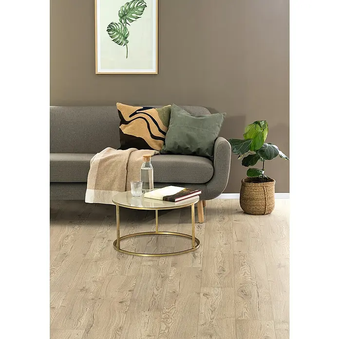Egger Laminat NatureSense Aqua - Olchon Eiche sandbeige, Landhausdiele, 1.292 x 193 x 8 mm - Ein gemütliches Wohnzimmer mit einem grauen Sofa, Kissen und einem runden Tisch mit Dekorationen wie einer Wasserflasche.
