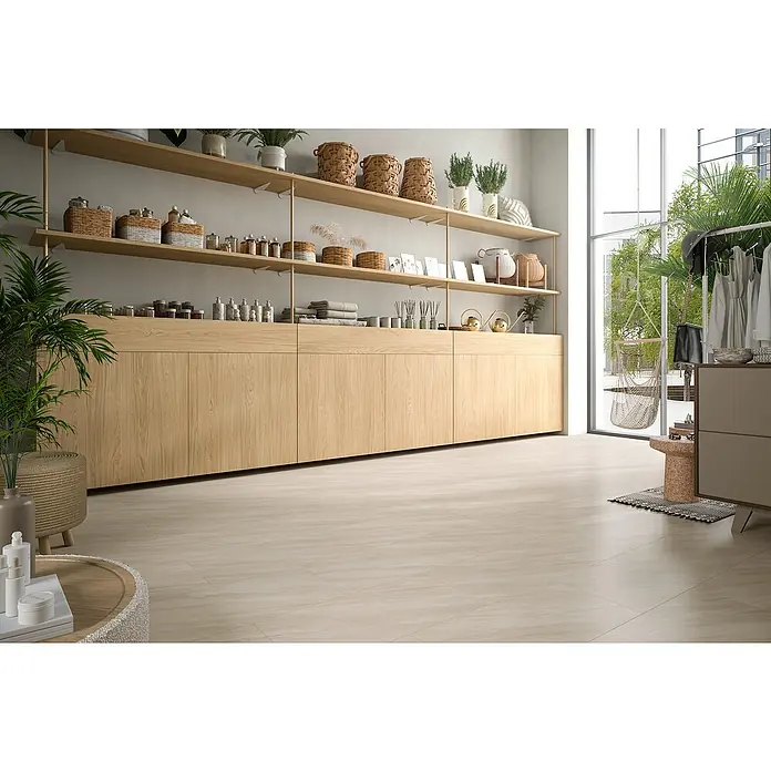 Egger Laminat NatureSense Aqua - Calvia Stein sandgrau, Fliese, 1.292 x 327 x 8 mm - Ein helles, modernes Interieur mit Holzregalen, Körben und Pflanzen. Der Boden ist hellbeige gefliest, was eine warme Atmosphäre schafft.