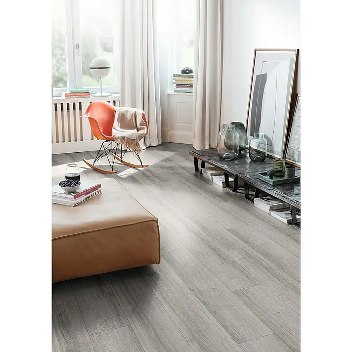 Egger Laminat NatureSense Aqua - Sherman Eiche hellgrau, Landhausdiele, 1.292 x 193 x 8 mm - Ein modernes Wohnzimmer mit hellem Holzboden, einem braunen Ledersofa und einem orangefarbenen Schaukelstuhl, der eine warme, einladende Atmosphäre schafft.