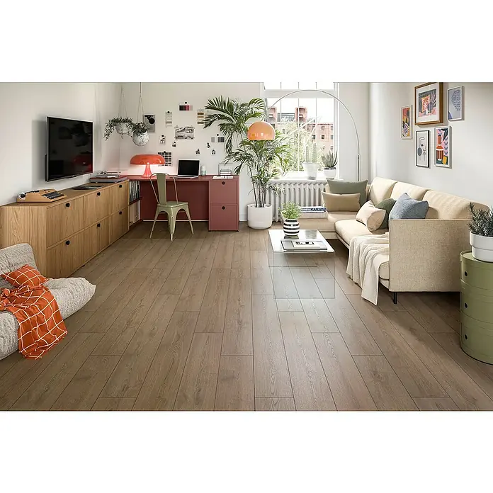 Egger Laminat NatureSense Aqua - Turin Eiche braun, Landhausdiele, 1.292 x 193 x 8 mm - Einladendes Wohnzimmer mit Holzboden, bequemer Couch, Schreibtischbereich und grünen Akzenten, die eine warme und stilvolle Atmosphäre schaffen.