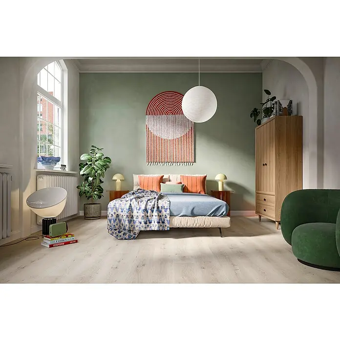 Egger Laminat NatureSense Aqua - Pinot Eiche weiß, Landhausdiele, 1.292 x 193 x 8 mm - Helles Schlafzimmer mit gemütlichem Bett, grünem Sessel und stilvoller Deko, die eine entspannende Atmosphäre schafft. Das Bett ist zentral.