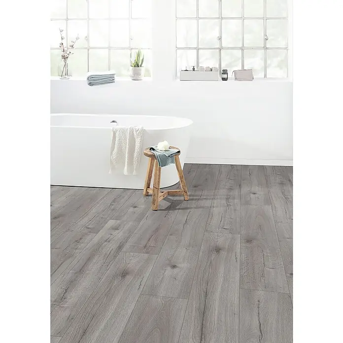 Egger Laminat NatureSense Aqua - Loja Eiche hellgrau, Landhausdiele, 1.292 x 246 x 8 mm - Ein modernes Badezimmer mit grauem Holzboden, einer freistehenden Badewanne und einem Holzhocker. Schönes Design und hochwertige Materialien.