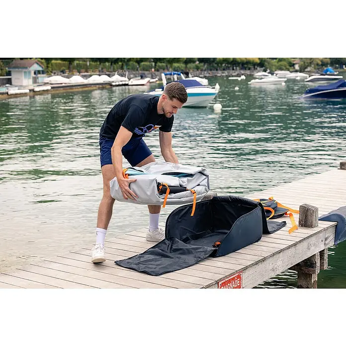 Sevylor Kajak Colorado Kit - L x B: 342 x 96 cm, Nutzlast: 180 kg, Geeignet für: 2 Personen - Ein Mann packt ein hellgraues, zusammengefaltetes SUP Board auf einem Holzsteg neben einer schwarzen SUP Board Tasche aus.