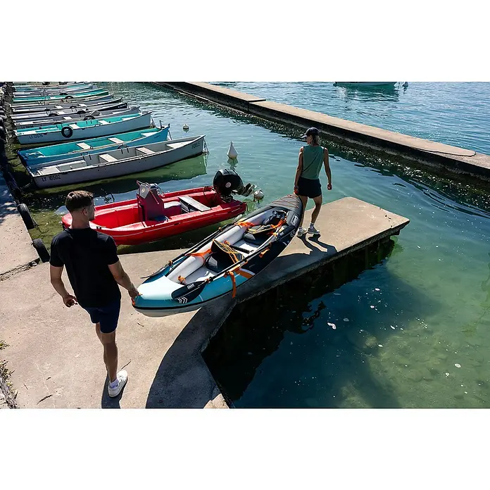 Sevylor Kajak Colorado Kit - L x B: 342 x 96 cm, Nutzlast: 180 kg, Geeignet für: 2 Personen - Zwei Personen tragen ein Coleman Kajak zu einem Anlegesteg mit Booten im Hintergrund. Das aufblasbare Kajak ist ideal für Seen und ruhige Flüsse.
