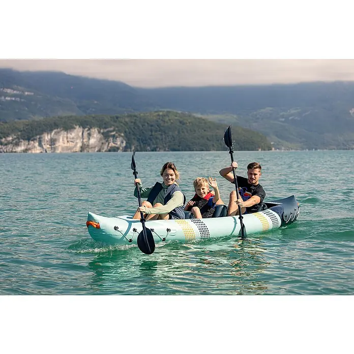 Sevylor Kajak Toledo - L x B: 361 x 90 cm, Nutzlast: 200 kg, Geeignet für: 2+1 Personen - Familie genießt eine entspannte Paddeltour mit einem blauen, aufblasbaren Kajak auf einem ruhigen See vor einer Bergkulisse.