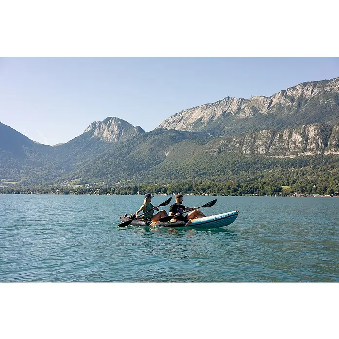 Sevylor Kajak Colorado Kit - L x B: 342 x 96 cm, Nutzlast: 180 kg, Geeignet für: 2 Personen - Zwei Personen paddeln mit einem aufblasbaren Kajak auf einem ruhigen See, im Hintergrund malerische Berge.