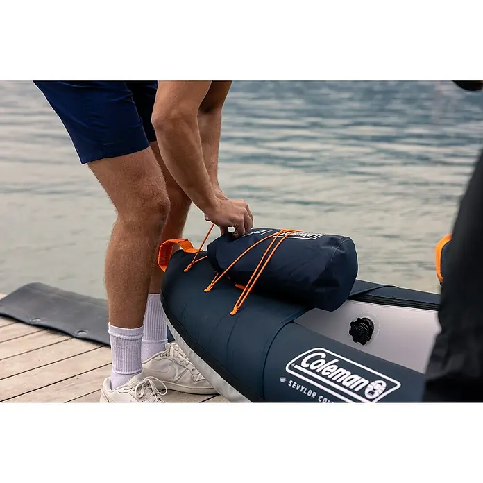 Sevylor Kajak Colorado Kit - L x B: 342 x 96 cm, Nutzlast: 180 kg, Geeignet für: 2 Personen - Eine Person befestigt eine wasserdichte Tasche mit einem orangefarbenen Bungee-Seil an einem Coleman Sevylor Collapsible Kajak.