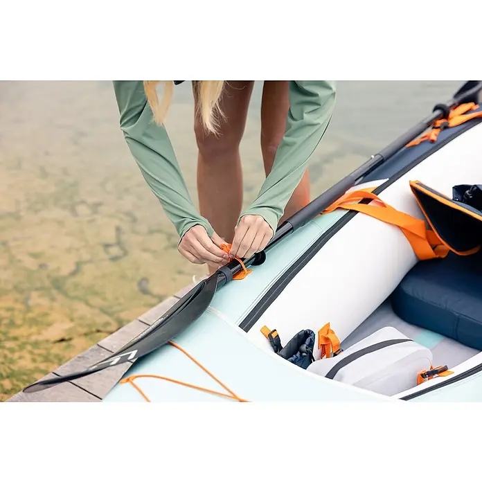 Sevylor Kajak Maui 2 + 1 - L x B: 380 x 98 cm, Nutzlast: 250 kg, Geeignet für: 2+1 Personen - Eine Person befestigt ein schwarzes Paddel an einem aufblasbaren Kajak mit orangefarbenen Riemen, wodurch die Ausrüstung für das Paddeln gesichert wird.