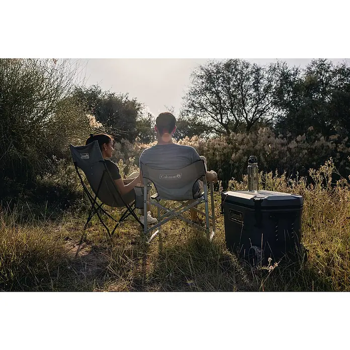 Coleman Kühlbox Convoy QT65 - L x B x H: 38 x 73 x 47 cm, Schwarz, 66 l - Ein Paar entspannt in Coleman Campingstühlen im Freien, neben einer Coleman Kühlbox und einer Wasserflasche.